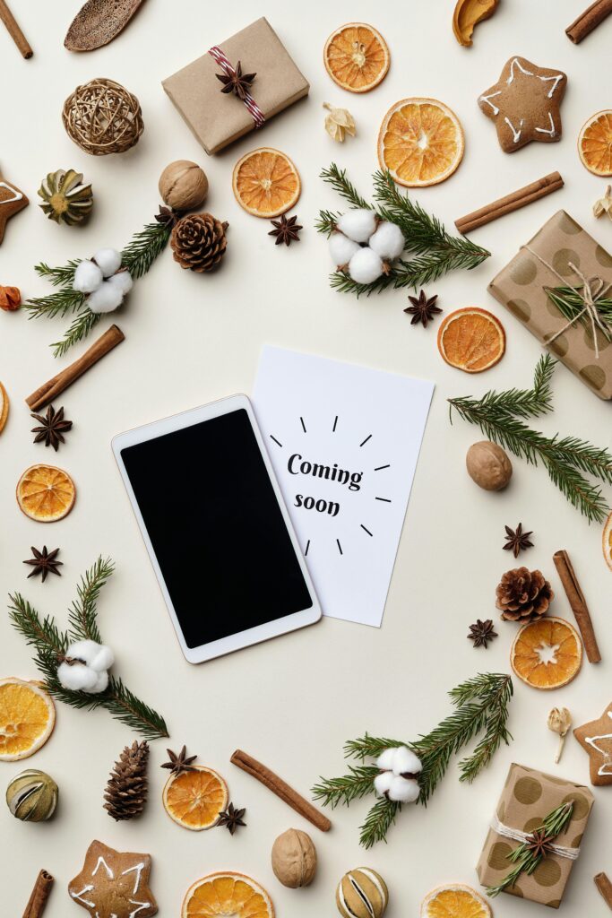 Flatlay featuring holiday decorations with gifts, spices, and a tablet on a light background.